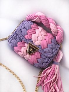 a pink and purple purse sitting on top of a white table next to a gold chain