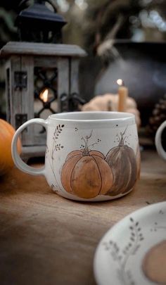 there is a coffee cup with pumpkins painted on it and candles in the background