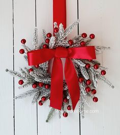 a christmas wreath hanging on the side of a white wall with red ribbon and decorations