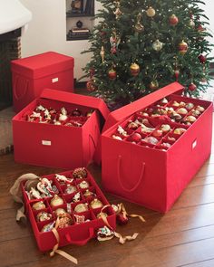 three red boxes filled with ornaments next to a christmas tree