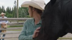 a woman standing next to a black horse near a man in a cowboy hat and jeans