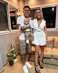 a man and woman standing next to each other in front of a couch with a baby