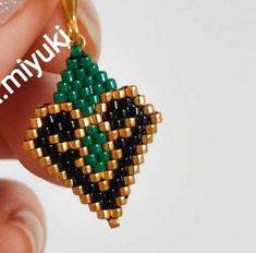 a hand holding a small beaded pineapple charm in gold and green colors with the words tinyki on it