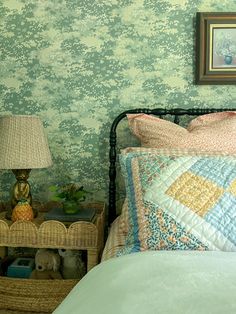 a bed in a bedroom with green wallpaper next to a night stand and lamp