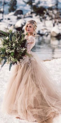 a woman in a wedding dress holding a bouquet standing in the snow with mountains in the background