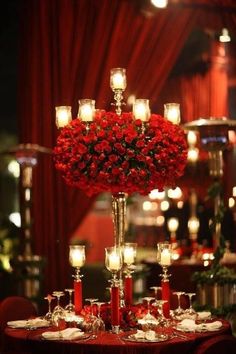 a centerpiece with candles and roses on a table in a room filled with red drapes