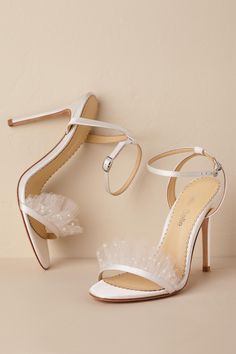 a pair of white high heeled shoes with ruffles on the ankle straps