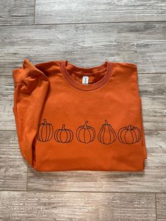 Stay cozy and stylish with our Row of Pumpkins tee. Crafted from a soft cotton blend and featuring an eye-catching pumpkin graphic, this long-sleeved tee shirt is perfect for fall. Enhance your wardrobe with a cozy, cute shirt to wear to all your fall festivities! TShirt with Pumpkins Long Sleeve TShirt Fall Shirt Womens Clothing Thanksgiving TShirt Holiday TShirt Please refer to the attached sizing chart CARE INSTRUCTIONS: Turn inside out to wash.   Do not bleach.  Do not dry clean.  Do not iro Fall Shirt Ideas, Pumpkin Graphic, Fall Festivities, Shirt Stays, Cute Shirt, Fall Shirt, Long Sleeve Tee Shirts, Fall Festival, Stay Cozy