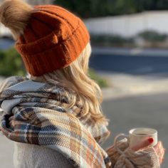 a woman holding a coffee cup in her right hand and wearing a plaid scarf around her neck