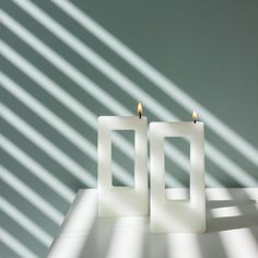 two candles sitting on top of a table in front of a shadow from the wall