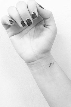 a black and white photo of a woman's arm with a small wave tattoo on it