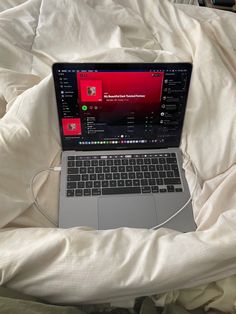 an open laptop computer sitting on top of a white bed covered in sheets and blankets