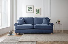 a blue couch sitting on top of a wooden floor next to a white rug and window