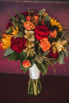 a bouquet of flowers in a white vase on a table with red and yellow flowers