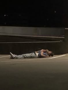 two people laying on the ground in an empty parking lot at night with their arms around each other