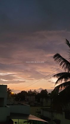 the sun is setting over some buildings and palm trees in the foreground, with dark clouds overhead