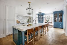 a large kitchen with blue cabinets and marble counter tops, along with bar stools