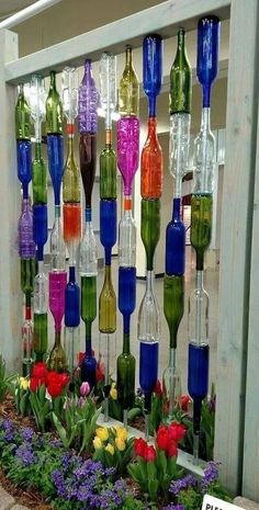 there are many different colored wine bottles hanging on the wall and in front of flowers