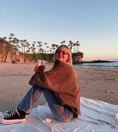 a woman sitting on the beach holding a drink