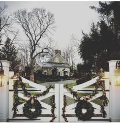 a white gate with wreaths and lights at the entrance to a large house in winter