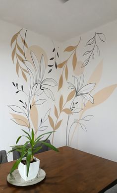 a wooden table topped with a potted plant next to a white wall painted with leaves