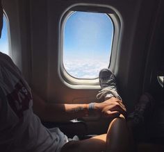 a man sitting on an airplane seat with his feet up in the air and looking out the window