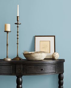 a wooden table topped with a bowl next to a candle holder and two framed pictures