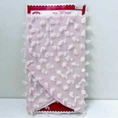 the pink and white blanket has pom - poms on it's edges