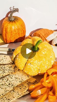 an assortment of cheeses and crackers on a plate with pumpkins in the background