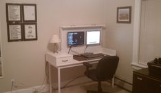 a white desk with a computer on top of it in front of a wall mounted pictures