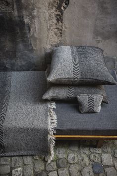 two gray and black pillows sitting on top of a bench next to a stone wall