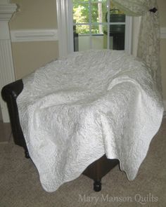 a bed with a white bedspread on top of it in front of a window