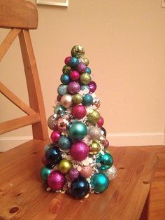 a small christmas tree made out of ornaments sits on a wooden table next to a chair