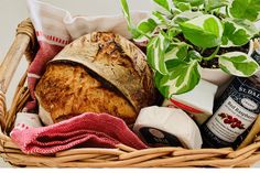 a basket filled with bread, cheese and other items next to a potted plant