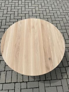 a round wooden table sitting on top of a brick floor next to a parking lot