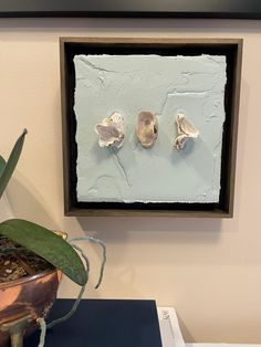 two small pieces of art hanging on the wall next to a potted plant in front of it