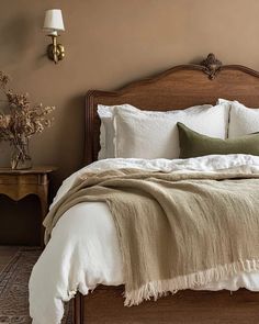 a bed with white linens and pillows in a brown room next to a lamp