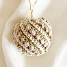 a crocheted ornament hanging on a white cloth with gold chains and beads