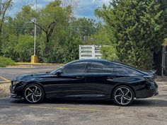 a black sports car parked in a parking lot next to some trees and bushes on a sunny day