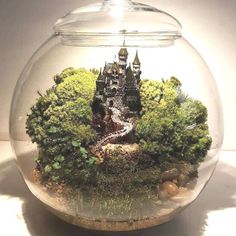 a glass bowl filled with water and moss covered in rocks, trees and a castle