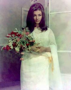 a woman holding a bouquet of flowers in front of her face and wearing a white dress