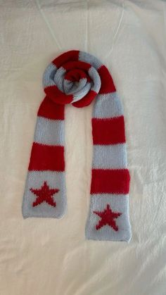 a red and white scarf with stars is laying on top of a bed, it has a knot in the middle