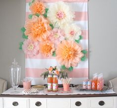 a table topped with lots of drinks and flowers on top of a white dresser next to a striped wall