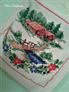 a cross stitched picture of a house and trees on a white cloth with red trim