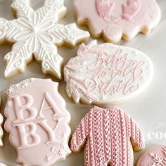 decorated baby cookies are displayed on a white tablecloth with snowflakes in the background