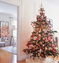 a decorated christmas tree in the corner of a living room with white walls and wood floors