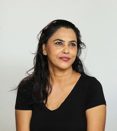 a woman with long black hair wearing a black shirt and smiling at the camera while standing in front of a white background