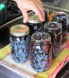 a person reaching for blueberries in a jar on a tray with other mason jars