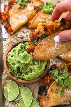 someone dipping guacamole into a wooden bowl with tortilla chips and lime wedges