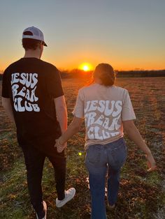 two people holding hands while walking in an open field at sunset with the sun setting behind them